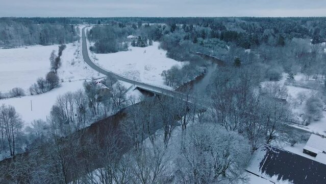 Snowy landscape with Abava river near Renda village (Kuldiga parish, Latvia) during winter, aerial view, moving forward, tilt down