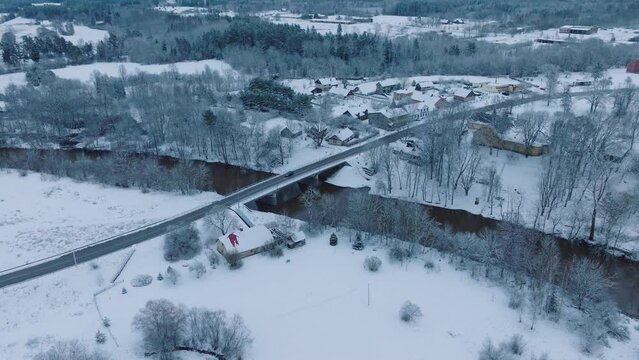 Snow-covered landscape of Abava river Renda village (Kuldiga parish, Latvia), aerial view, serene winter day, moving forward, tilt down