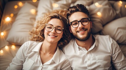 Happy western couple in glasses lying on the bed - obrazy, fototapety, plakaty