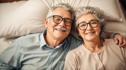 Happy senior couple in glasses lying on the bed - obrazy, fototapety, plakaty