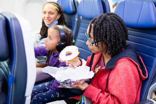 Teen sitting on a plane eating a bage.l