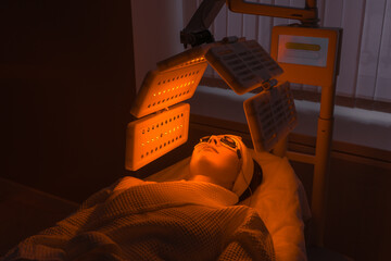 An elderly woman undergoes a facial rejuvenation procedure. Woman face lt Red light treatment At...