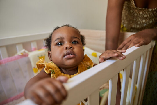 A baby toddler girl holding herself up while inside her crip