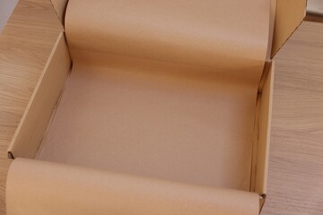 Empty cardboard box with kraft paper on wooden table. Delivery service
