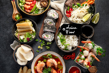 Traditional Asian food table. Spring roll, rice, shrimp, sushi, vegetables, meat on dark background