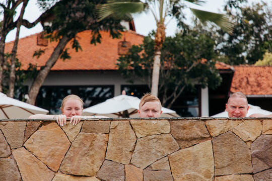 Three people peeping over the edge of a swimming pool.