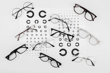 Vision test charts and glasses on white background, flat lay