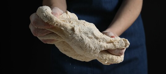 Making bread. Woman kneading dough on dark background, closeup