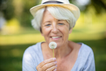 happy elderly woman senior blowing on a dandelion