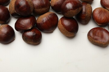 Sweet fresh edible chestnuts on white marble table, top view. Space for text