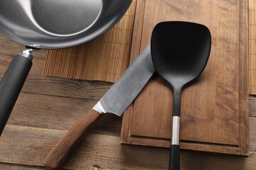 Black metal wok, knife and spatula on wooden table, above view