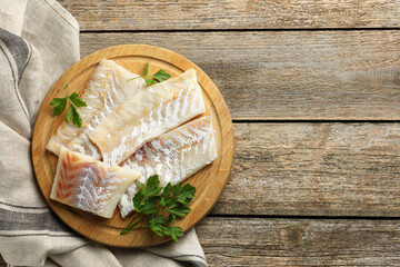 Fresh raw cod fillets and parsley on wooden table, top view. Space for text