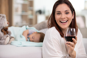 young mum holds a glass of wine while baby sleeps