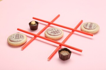 Tic tac toe game made with cookies and sweets on pink background