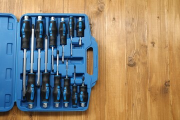 Set of screwdrivers in open toolbox on wooden table, top view. Space for text