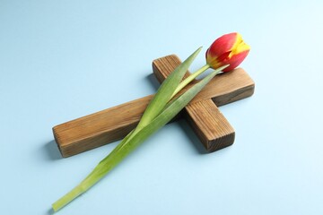 Easter - celebration of Jesus resurrection. Wooden cross and tulip on light blue background, closeup