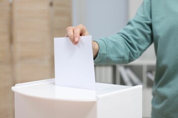 Woman putting her vote into ballot box on blurred background, closeup