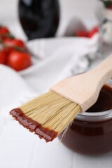 Marinade in jar and basting brush on white table, closeup