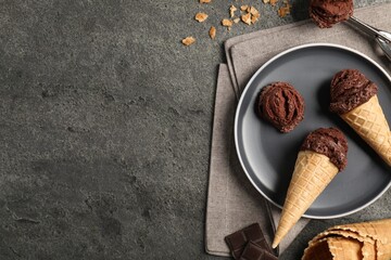 Chocolate ice cream scoops in wafer cones on gray textured table, flat lay. Space for text