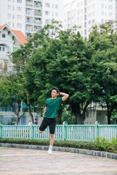 Young man stretching bodies, warming up for jogging in public park.