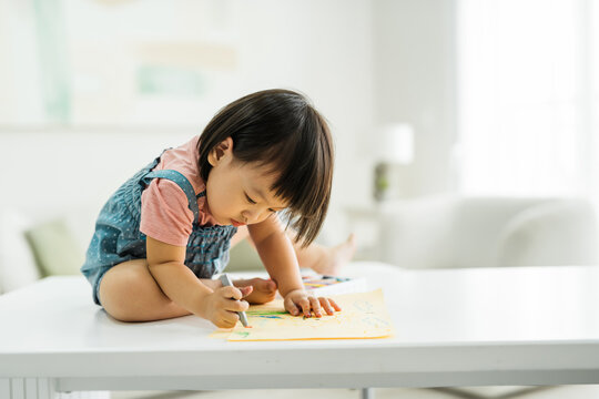 Cute little toddler girl drawing with crayons colour on the notebook