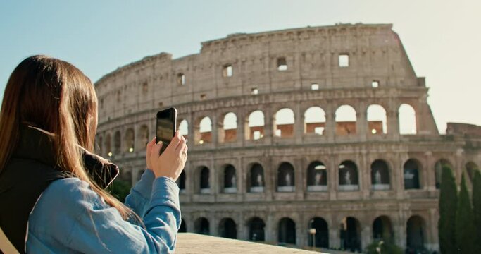 A beautiful tourist walking through the streets of Rome takes a photo near the Colosseum. Lifestyle videos of vacations and weekends, excursions and commemorative photos near ancient Roman ruins.
