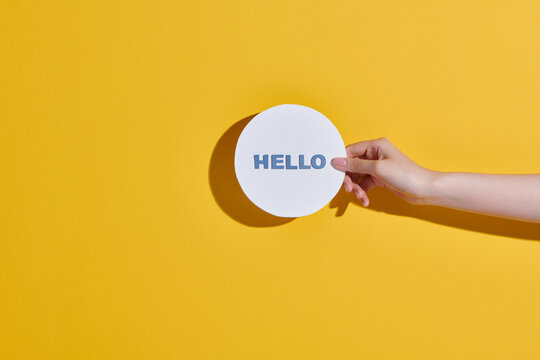 People hand holding circle of white paper with "Hello" written
