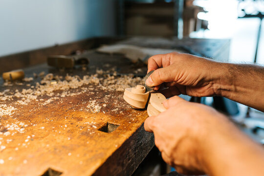 Faceless artisan carving violin scroll at workbench