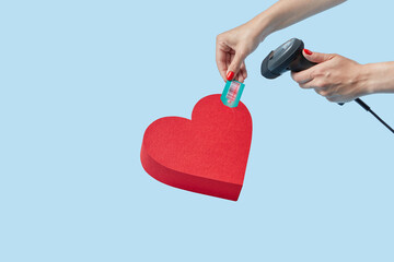 Hands of woman scanning barcode of red heart-shaped box.