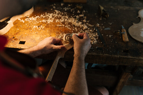 Crop craftsman carving violin scroll on workbench - Powered by Adobe