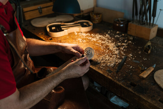 Faceless luthier making violin scroll in workshop