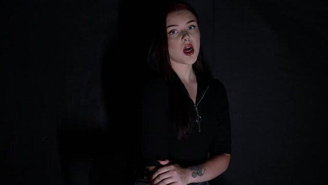 Attractive young Caucasian woman singing in front of black background while being lit in white light