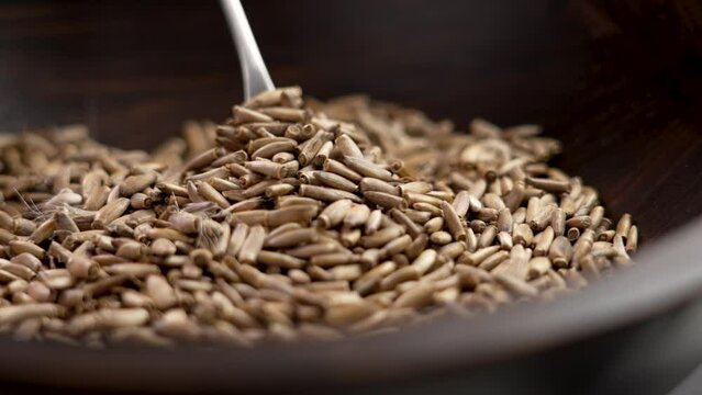 Process of making a decoction of milk thistle. A metal spoon picks up dried seeds from a wooden bowl in close up