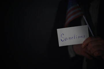 Man showing sanctions word on paper and devastated middle aged caucasian man in a black suit composition with dramatic lighting