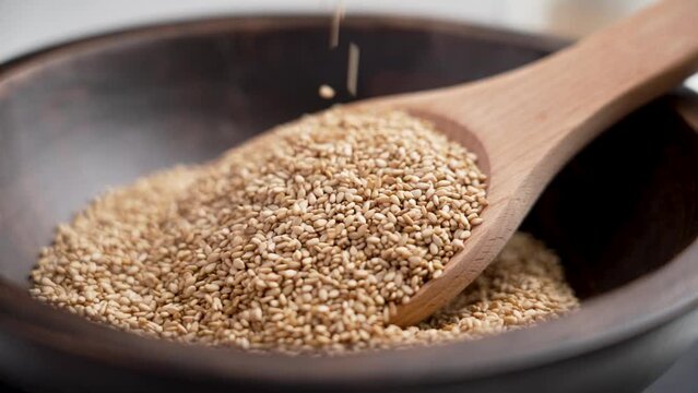 White sesame seeds falling on a wooden spoon in rustic bowl. Slow motion. Traditional Indian spices. Rotation. Contemplative video shot