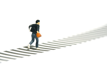 Miniature tiny people toy photography. Back side view of a boy pupil student running on zebra crossing crosswalk. Isolated on a white background
