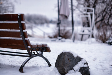 park bench on a winter alley at snowfall. bench with snow after snowstorm or in snow calamity in...