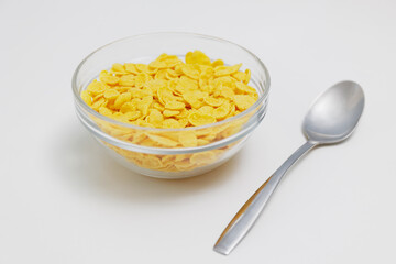 Corn flakes served in glass bowl with spoon on white