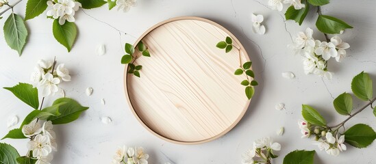 A circular wooden plate is placed in the center, decorated with an arrangement of delicate white flowers and fresh green leaves. The flat lay mockup offers a serene backdrop for any text or design - Powered by Adobe