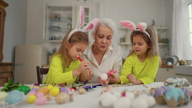 Easter grandmothers with granddaughters. Smiling grandmother with twins grandchildren painting decorating eggs in rabbit bunny ears, celebrate together at home. Easter, cheerful holiday concept.
