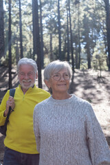 Happy senior couple walking in the forest holding hands enjoying vacation freedom and nature hiking in a sunny day in the woods
