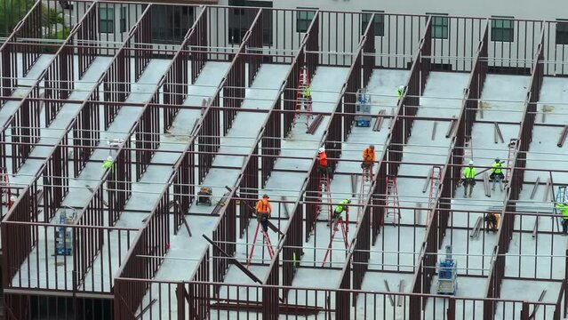 Construction works on metal walls of commercial building. Blue collar workers at large site with scattered equipment. Development of residential housing in America. Real estate market in USA.