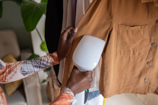 Black woman using handheld steamer on clothes