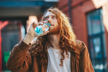 Young red haired man is holding a bottle of water, healthy lifestyle concept.