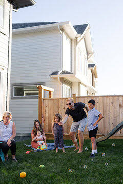 Adults and kids playing bocce ball outside in the backyard.