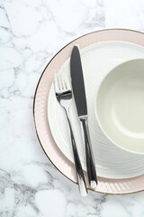Clean plates, bowl and cutlery on white marble table, top view