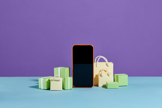 Parcel boxes and shopping bags near smartphone on color background