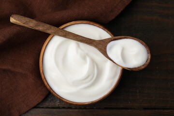 Delicious natural yogurt in bowl and spoon on wooden table, top view