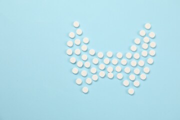 Endocrinology, Shape of thyroid gland made of pills on light blue background, flat lay. Space for text
