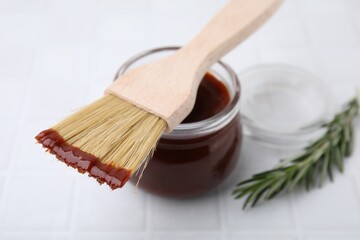 Marinade in jar and basting brush on white table, closeup